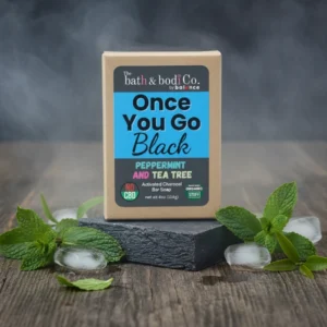 Balence Once You Go Black Peppermint & Tea Tree solid black soap bar with label, surrounded by fresh mint leaves, tea tree sprigs, and ice cubes on rustic wood.