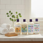 Four Balence shampoo & body wash bottles — Healing Tree, Kumquat, Monkey Farts, and Stress Relief — displayed together on a bathroom counter with towels, eucalyptus sprigs, and a loofah, in bright natural light.