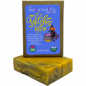 Balence Witch’s Brew handmade soap bar on an aged wooden table with candles, herbs, cinnamon sticks, and wisps of smoke creating a mystical atmosphere.