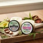 Two Balence Hemp Shea Butter jars—classic Shea Butter with hemp CBD and Ultimate Butter (Shea, Avocado, Kokum, 250 mg hemp CBD)—side by side on a rustic wooden tray with shea nuts, fresh avocado slices, kokum fruit, and hemp leaves, softly lit by morning sunlight for a clean, spa-like vibe.