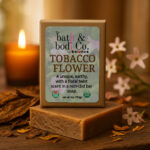 Balence Tobacco Flower handmade soap bar on a rustic wooden surface with dried tobacco leaves, delicate blossoms, calendula petals, and warm amber candlelight in the background.
